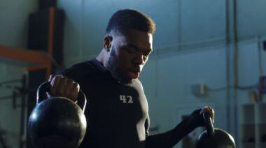 A person wears a black t-shirt with the number 42 on the chest while performing double kettlebell biceps curls.