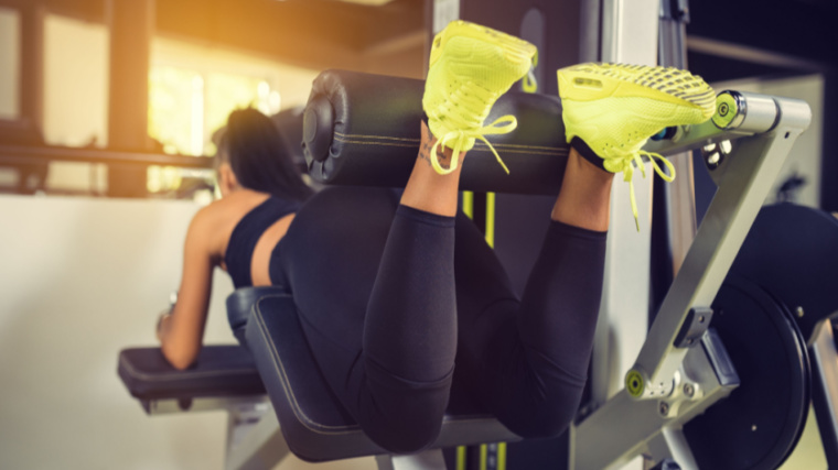 A person performs a prone hamstring curl while wearing neon yellow shoes.