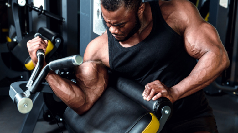 A person wearing a black tank top performs a unilateral cable preacher curl.