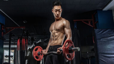 A shirtless person looks at their biceps as they perform an EZ-bar biceps curl.