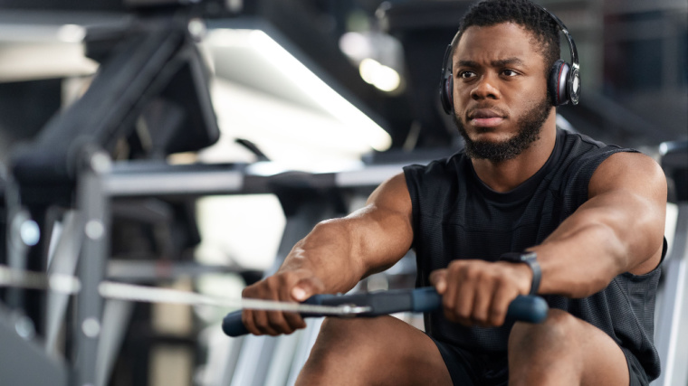 A person wearing a black tank top and headphones rows on a rowing machine.