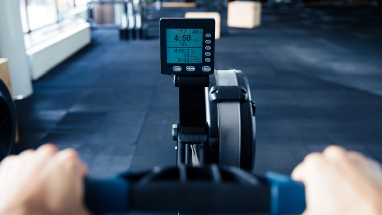 A close-up of a rowing machine screen shows a person rowing at a pace of 4:50/500-meters.