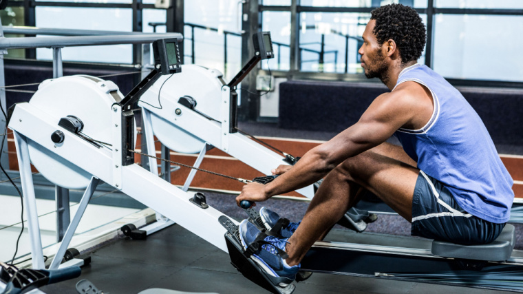 A person wearing a light blue tank top prepares to row on a machine.