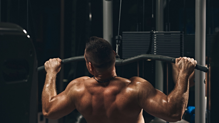 A shirtless person leans back as they perform a lat pulldown.