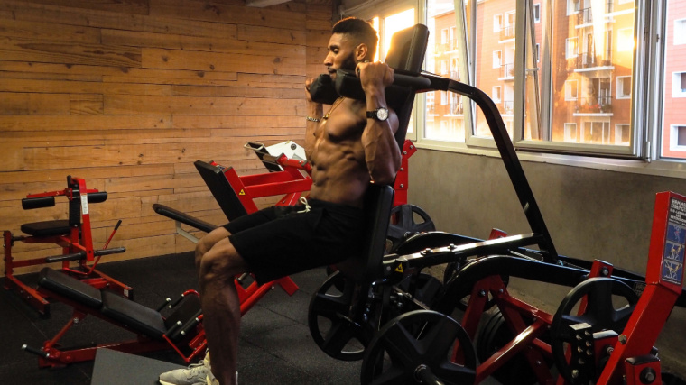 A shirtless person performs a hack squat on a machine.