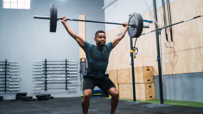 A person wearing an aqua t-shirt and shorts performs a snatch with a loaded barbell.