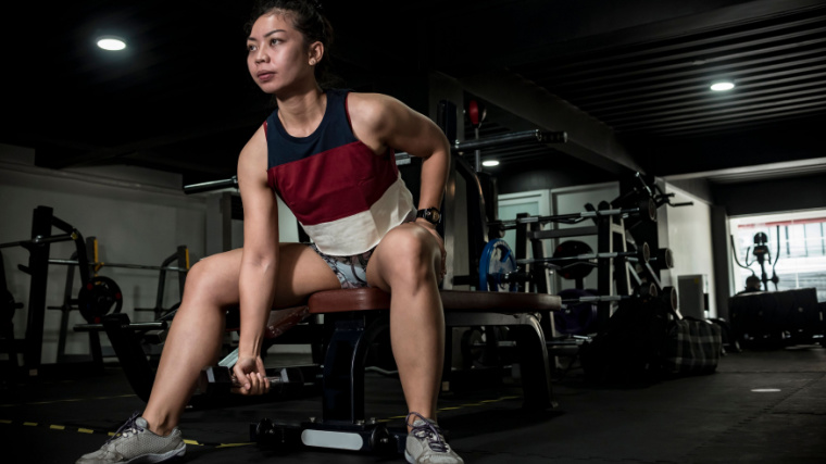 A person wearing a multi-colored tank top performs a concentration curl in the gym.