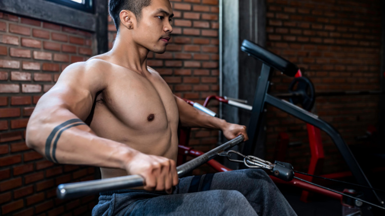 A shirtless person performs a wide-grip seated cable row.