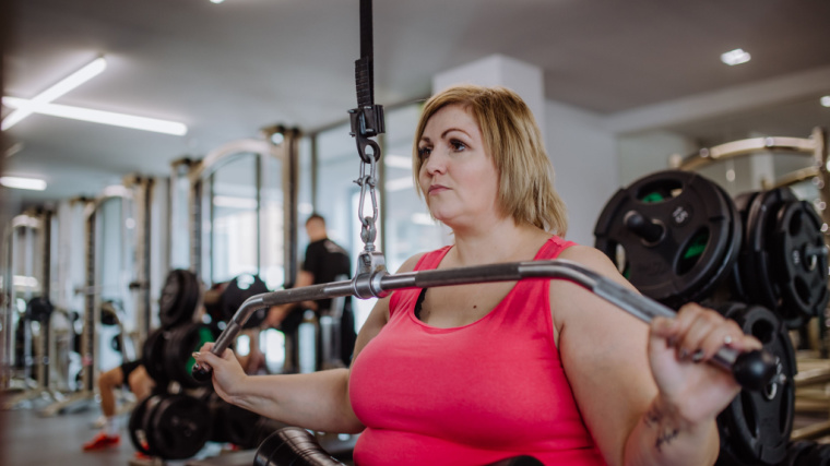 A person wearing a pink tank top performs a lat pulldown in the gym.