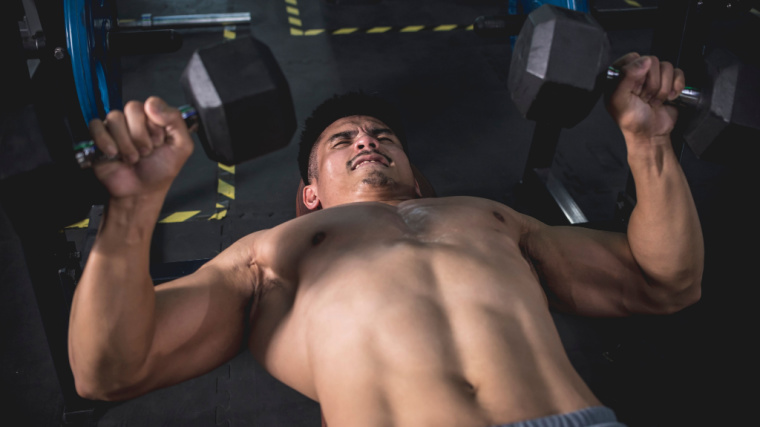 A shirtless person works hard to bench press two dumbbells.