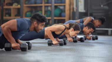 A class of four people perform dumbbell push-ups next to each other.