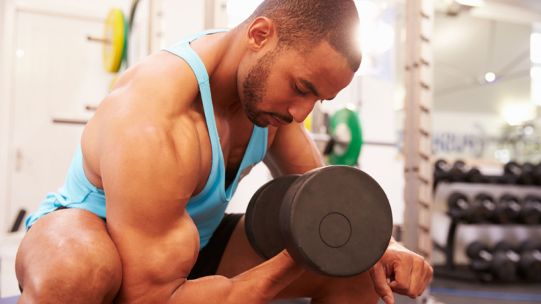 A person wearing a light blue tank top performs a concentration curl in the gym.