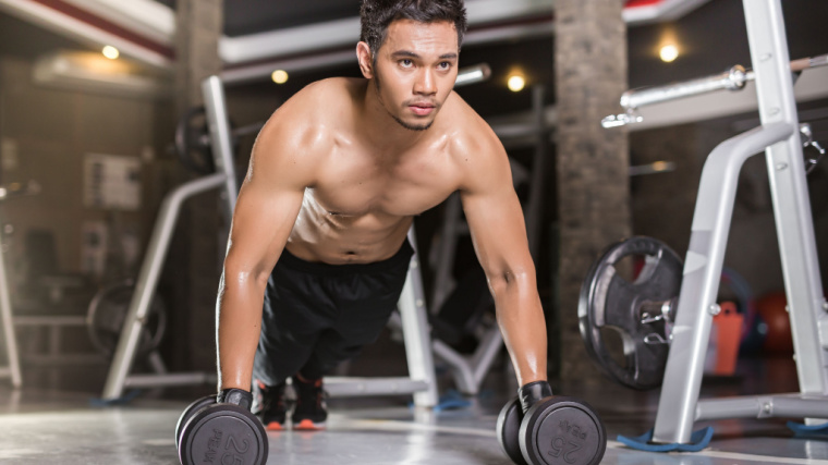 A shirtless person holds dumbbells as they perform a plank.