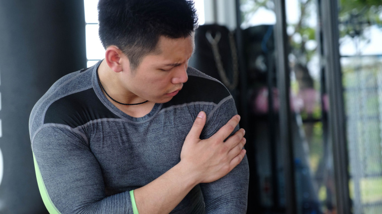 A person wearing a long-sleeved compression shirt touches their shoulder in pain in the gym.