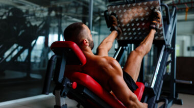 A shirtless person is shown performing a leg press from behind the machine.