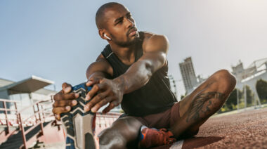 Sporty,Muscular,African,Male,Athlete,In,Earphones,Looking,Away,,Stretching