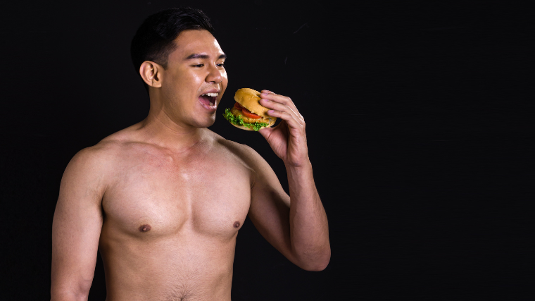 shirtless athlete enjoys burger