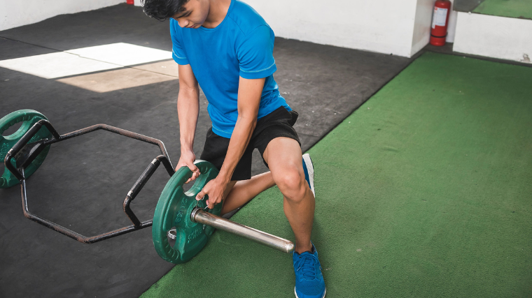 gymgoer loads plates onto an empty trap bar