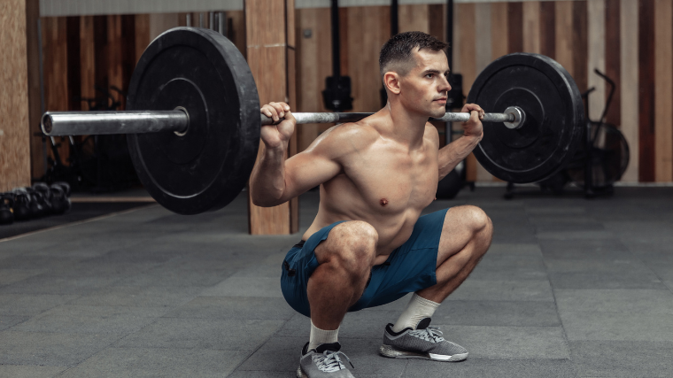 man sits into low back squat in gym