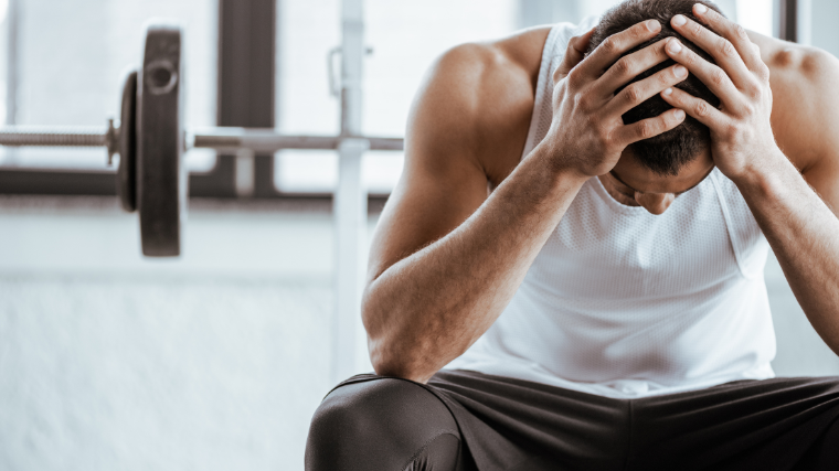 man sits frustrated on bench press with head in hands