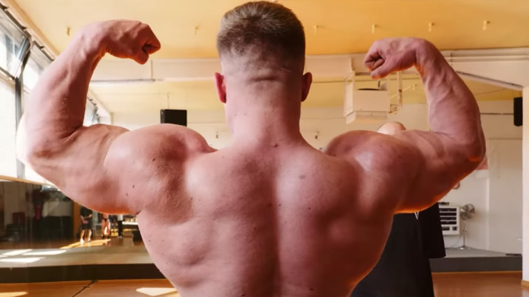 Shirtless bodybuilder posing with his back to the camera