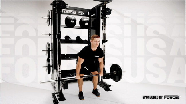 A person wearing a black shirt holds a barbell while facing outward from a Force USA Multi Trainer.
