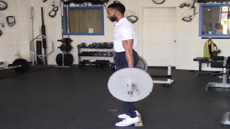 A person wearing a white polo stands up at the top of a barbell hack squat.
