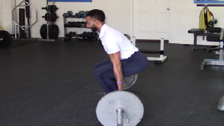 A person wearing a white polo performs a barbell hack squat.