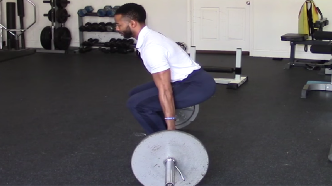 A person wearing a white polo performs a barbell hack squat.