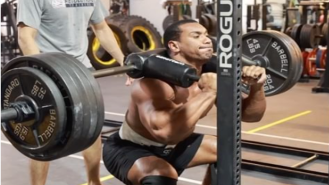 Larry Wheels performs a safety squat bar squat with his shirt off.