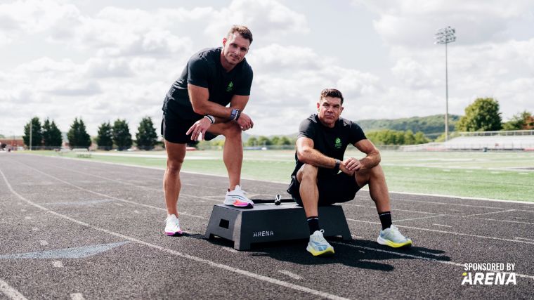 Two people look at the camera while sitting on an ARENA Platform on a track.