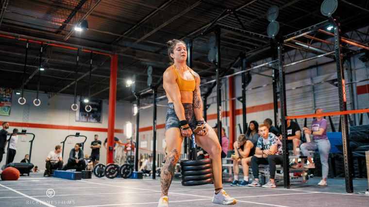 Person wearing orange tank top and black spandex duck-walking with loaded plates.