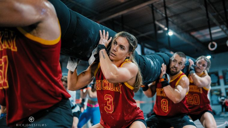 A team of CrossFitters wearing red jerseys squats with a sandbag.