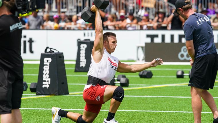 CrossFitter Samuel Cournoyer lunging with a single dumbbell over his head.