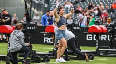CrossFitter Emma Lawson raises both of her hands overhead in a celebration on a turf field.