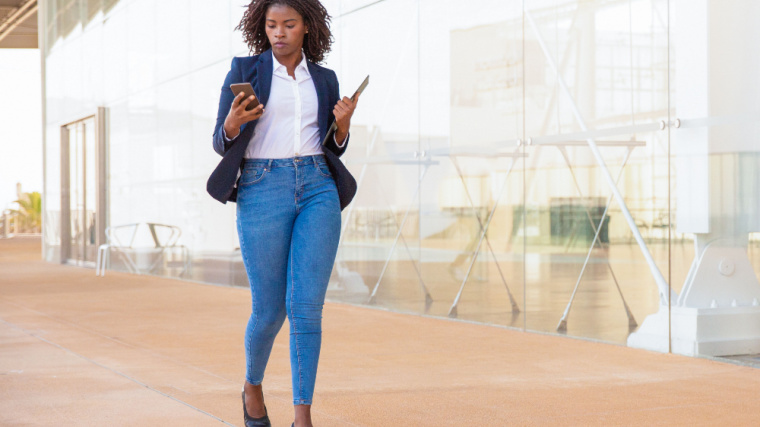 A business professional walks outside while texting.