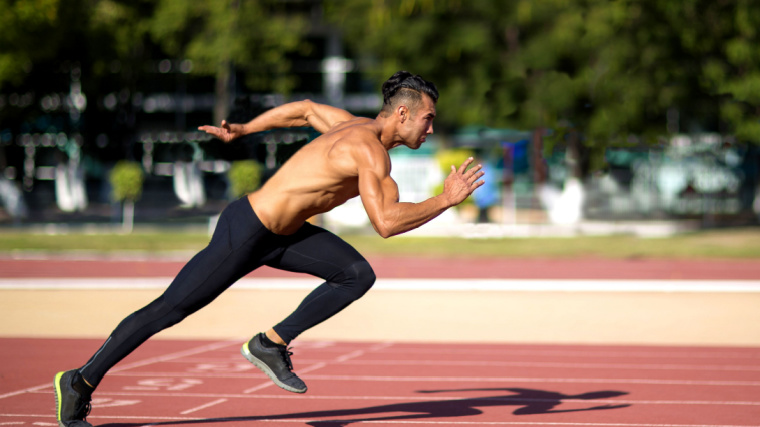 A shirtless athlete sprints down an outdoor track.