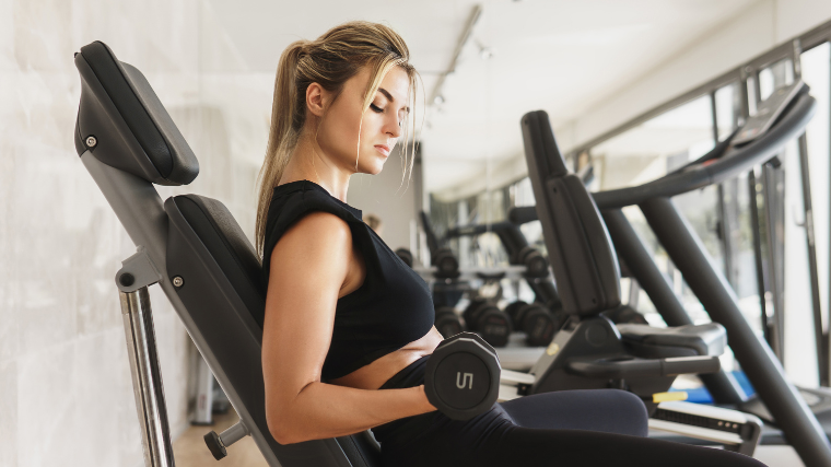 woman performs dumbbell curl on incline bench