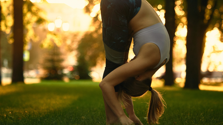 A woman outdoors performing the yoga forward fold.