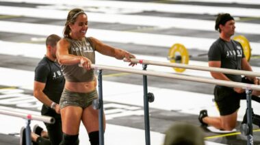 CrossFit athlete grips a pair of dip bars with both hands.
