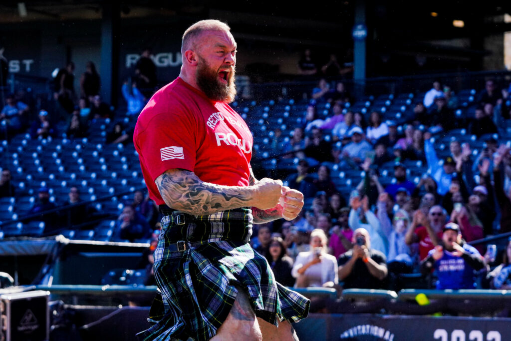 Strongman Hafthor roaring and pumping his fist, wearing a red Rogue t-shirt and a kilt.