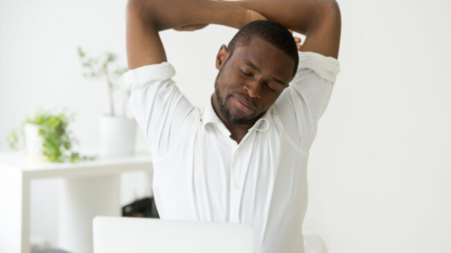 A person stretches their arms at their home office desk.