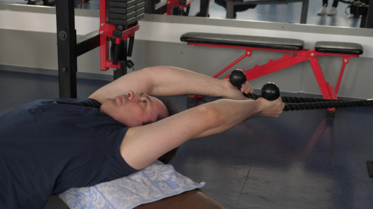 A person performs a cable pullover in the gym.