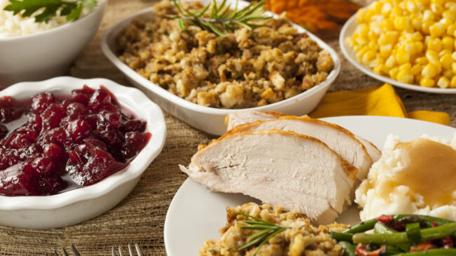 A table is loaded with Thanksgiving food, including slices of turkey, cranberry sauce, and stuffing.
