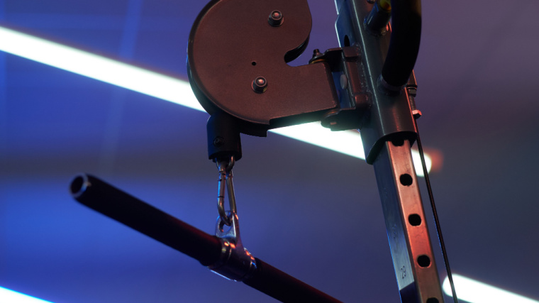 A straight cable bar hangs from a cable machine in the gym.