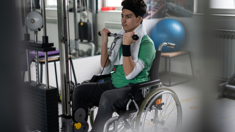 A person performs cable curls in the gym while using a wheelchair.