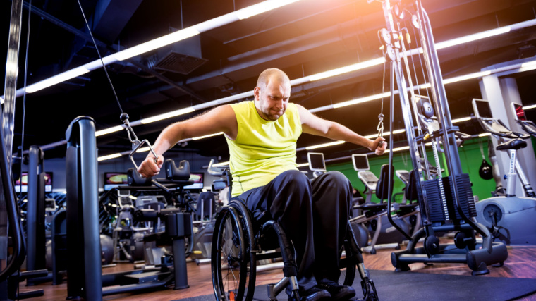 A person performs cable flyes in the gym while sitting in a wheelchair.