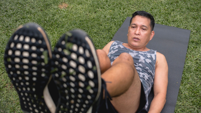 A person performs an ab exercise on turf in a gym.