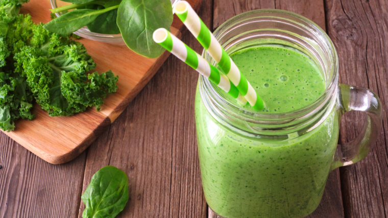 A green smoothie sits in a jar on a table with two paper straws.