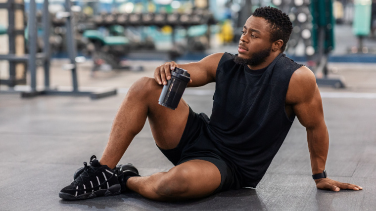 A person sits down in the gym and sips from a water bottle.